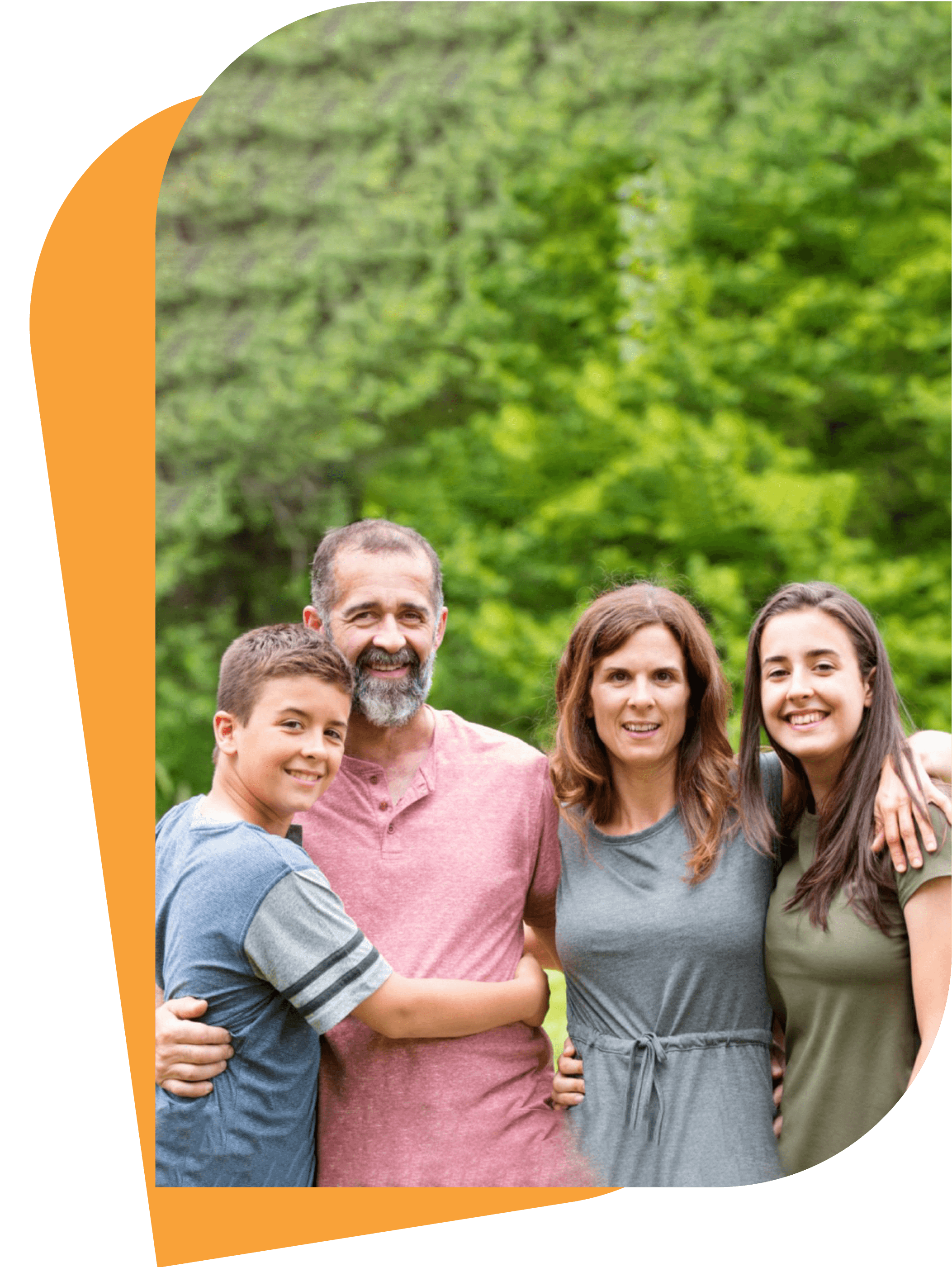 Happy family of four standing together outdoors, with lush green trees in the background.