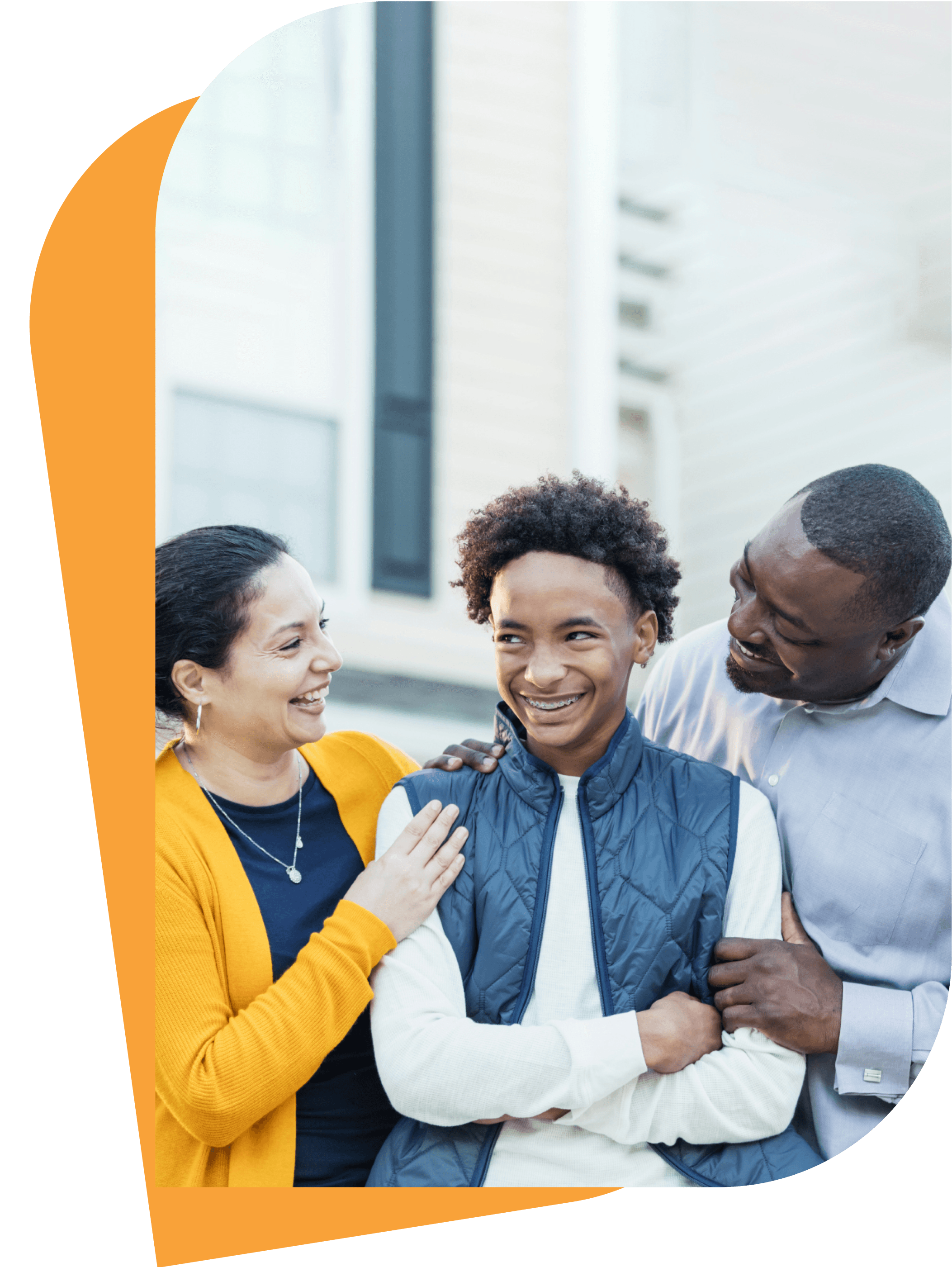 Happy family with parents smiling and embracing their teenage son outdoors.